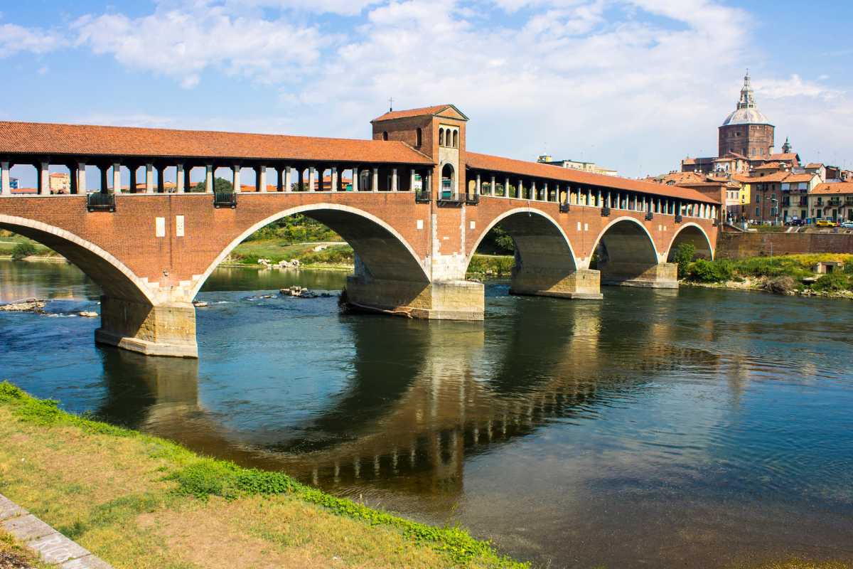 Veduta panoramica di Pavia con la Certosa e il Ponte Coperto, evidenziando l'architettura gotica e il fiume Ticino